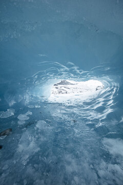 View of the vibrant blue ice cave walls and the snowy landscape visible through the natural opening in Skaftafell, Hornafjordur, Iceland.