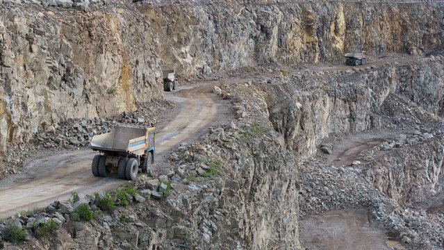 Aerial view of a porphyry open-pit mine with large dump trucks navigating the winding dirt roads along the steep rocky walls in Krakow, Lesser Poland Voivodeship, Poland.