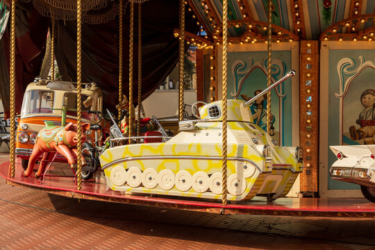 View of a vintage carousel featuring a tank-shaped ride, a pig figure, and other classic amusement park vehicles under warm lighting in Netherlands.