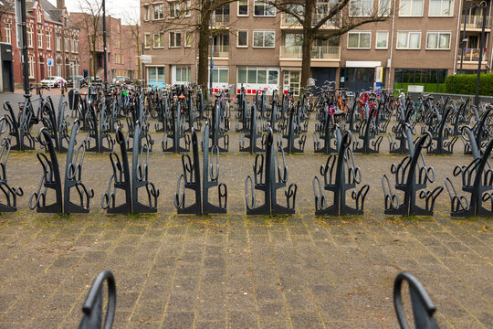 View of a large bicycle parking area with numerous metal racks and parked bicycles in front of residential buildings in the Netherlands.