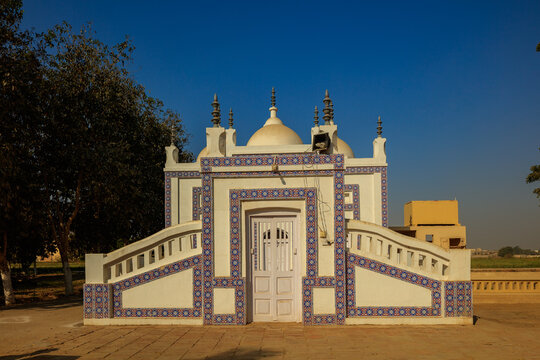 View of the historic white mausoleum with intricate blue tile patterns and a central dome, set against a clear blue sky in Hyderabad, Sindh, Pakistan.