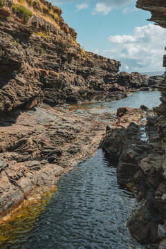 View of Cala des Murtar featuring rugged rocky cliffs, a narrow inlet of clear sea water, and a bright blue sky in Menorca, Islas Baleares, Spain.