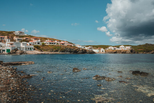 View of Cala des Murtar with white houses on the rocky coastline, clear blue water, and a bright sky in Illes Balears, Islas Baleares, Spain.