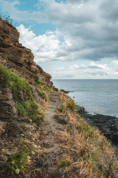 View of Cala des Murtar featuring a rugged coastal path along rocky cliffs overlooking the Mediterranean Sea with wild vegetation in Illes Balears, Islas Baleares, Spain.