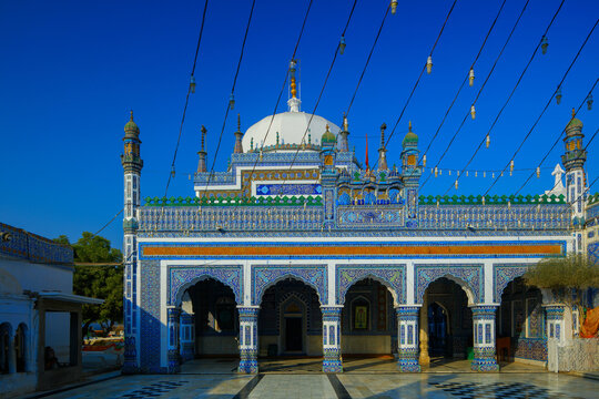 View of the ornate blue tile work and white dome of the Shah Abdul Latif Bhittai Shrine under a clear blue sky in Bhit Shah, Sindh, Pakistan.