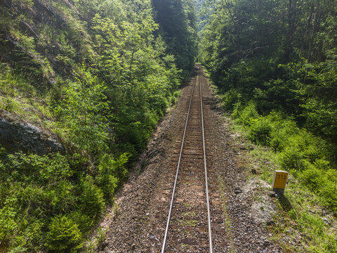 Aerial view of Bystricka dolina in Velka Fatra with railway tracks cutting through a dense green forest and rocky slopes in Dolny Harmanec, Banskobystricky kraj, Slovakia.