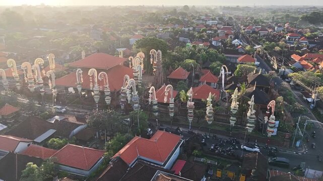 Aerial view of Pura Agung Petilan with traditional Balinese architecture and ornate penjor decorations in the urban landscape of Kecamatan Denpasar Timur, Bali, Indonesia.