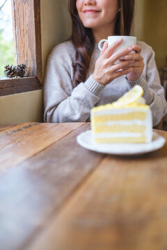 Vertical closeup image of a woman drinking coffee and eating a lemon cake in cafe