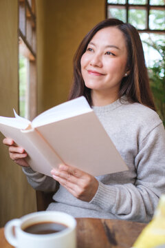 Vertical portrait image of a woman reading a book with coffee cup and a lemon cake on the table