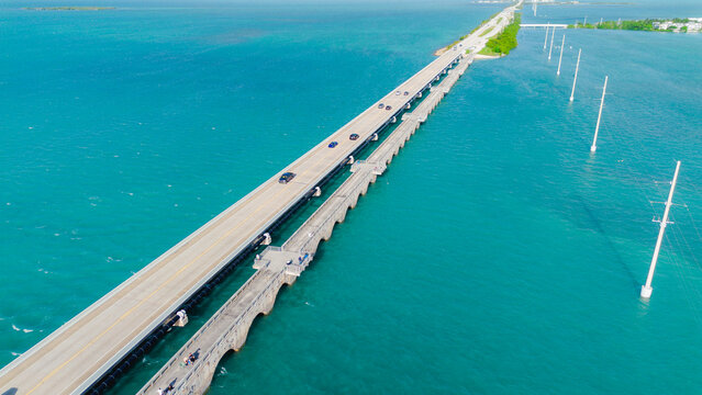 Aerial view of the Seven Mile Bridge spanning the turquoise waters of the Florida Keys with cars driving along the highway and utility poles in the sea, Key West, Florida, United States.