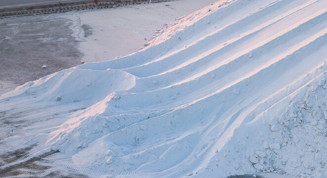 Aerial view of a sculpted sea salt stockpile with parallel harvesting tracks and layered white mineral formations creating an abstract geometric landscape during salt production in France.