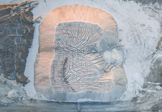 Aerial view of industrial sea salt stockpile with intricate heavy machinery tire patterns across its surface, captured in soft evening light France.