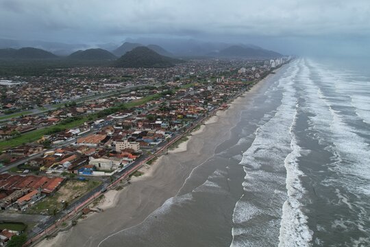 Aerial view of the coastal town with its sandy beach, residential buildings, and rolling hills under a cloudy sky in Mongagua, State of Sao Paulo, Brazil.