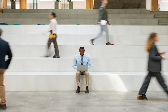 Focused businessman uses laptop on office stairs amidst rush