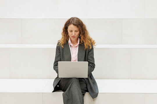 Businesswoman working on laptop on white minimalist staircase