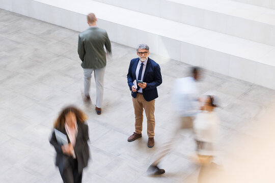 Focused businessman holds smartphone in modern office among crowd