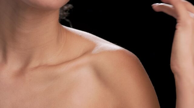 Big close-up shot of a light brown-skinned woman gently strokes her clavicles against black background | Balanced skin for beauty advertisement