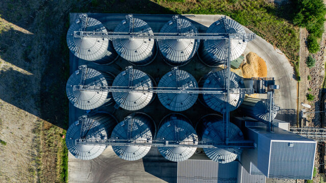 Aerial view of a large industrial facility featuring multiple metallic grain silos arranged in a grid pattern with connecting walkways and concrete ground in Beocin, Vojvodina, Serbia.