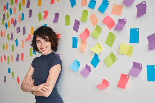 Smiling businesswoman stands by a wall with colorful adhesive notes