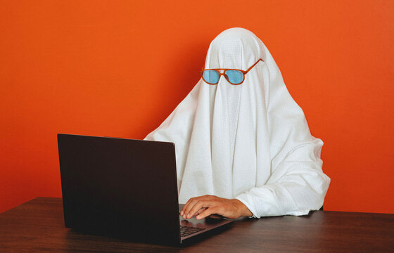 Man in ghost costume types on a laptop at the office