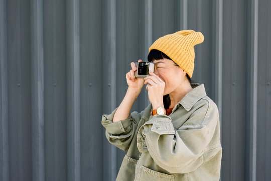 Urban hipster in casual outfit taking photo with analog camera outdoors