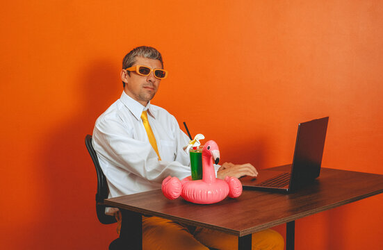 Man works on laptop with flamingo cocktail in orange office