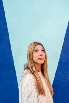 Woman in knit sweater looking up in front of colourful modern wall
