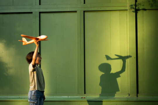 Boy walks in the park holding a toy airplane at sunset