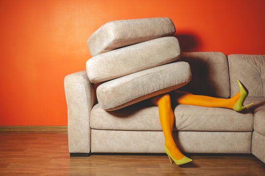Woman in yellow tights buried by sofa cushions in bright surreal living room