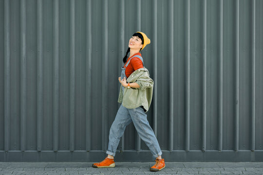 Laughing woman in casual hipster outfit walking by urban wall