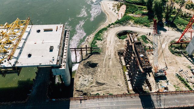 Aerial view of bridge construction over the Danube river, featuring concrete pillars, heavy machinery, and construction workers on the riverbank in Sremski Karlovci, Vojvodina, Serbia.