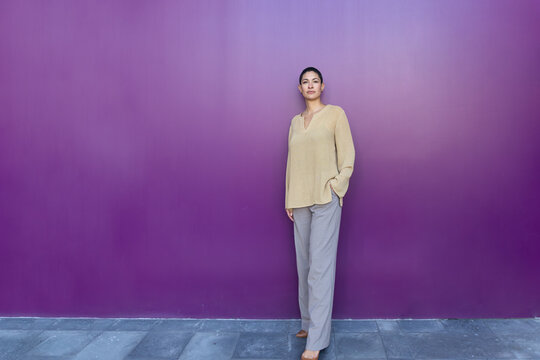 Confident business professional stands smiling by a purple wall