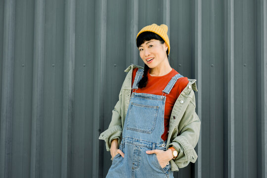 Smiling woman in casual denim outfit and beanie against urban wall