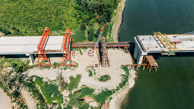 Aerial view of a bridge construction site with concrete segments and orange gantry cranes over the Danube river in Sremski Karlovci, Vojvodina, Serbia.