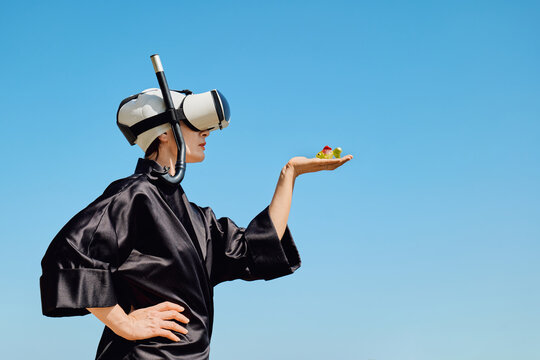 Woman in VR headset and snorkel holds plastic fish outdoors
