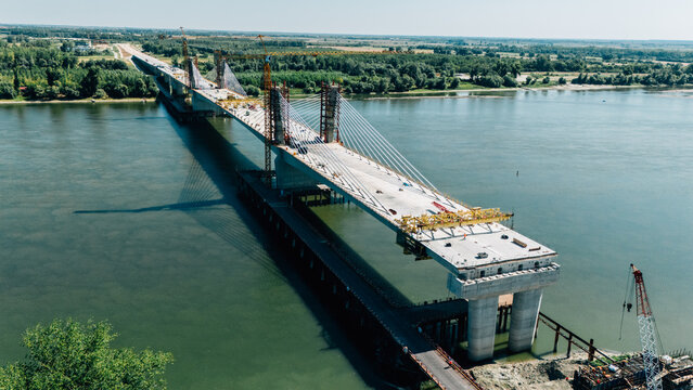 Aerial view of the bridge under construction spanning the Danube river with cranes and concrete pillars visible in Sremski Karlovci, Vojvodina, Serbia.
