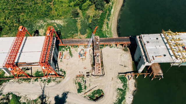 Aerial view of a bridge under construction with large orange cranes and concrete segments over a river in Sremski Karlovci, Vojvodina, Serbia.
