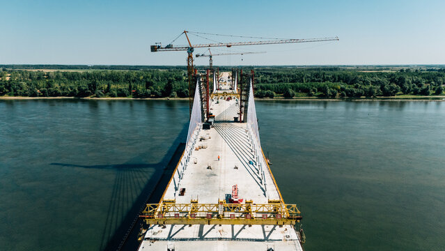 Aerial view of a cable-stayed bridge under construction with tall cranes and concrete deck spanning the river in Sremski Karlovci, Vojvodina, Serbia.