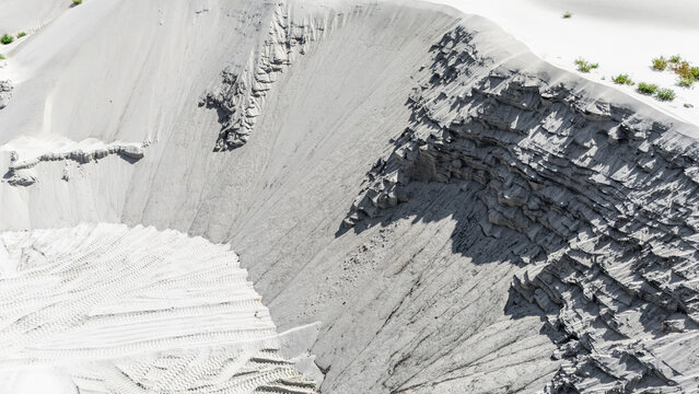 Aerial view of a large sand and gravel quarry with deep excavation layers, visible tire tracks on the sandy floor, and sparse vegetation on the edges in Novi Sad, Vojvodina, Serbia.