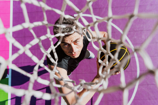 Male athlete dunks basketball on outdoor urban court
