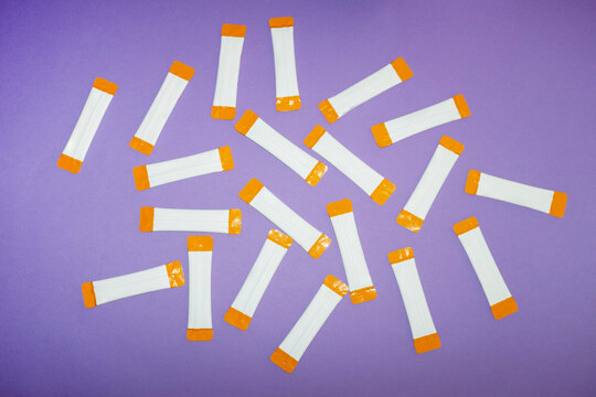 Vitamin supplement stick packs lie scattered on a purple background