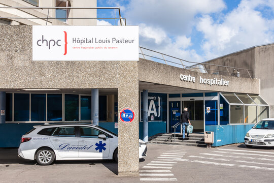 Cherbourg, France - July 20, 2026: A man holding a suitcase head for the entrance of the Louis Pasteur Hospital, part of the Cotentin Public Hospital Center, as a light medical vehicle is stationing.
