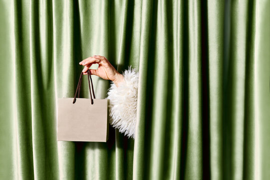 Female hand holds a gift bag through a green velvet curtain indoors