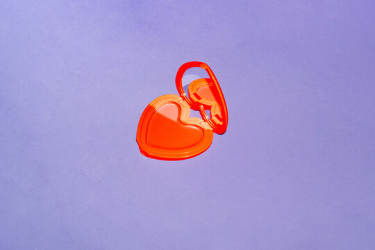 A red heart makeup compact rests on a purple background