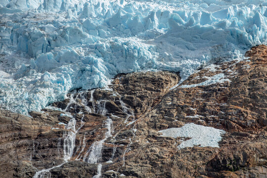 View of the glacier ice in Torres del Paine National Park with melting water streams cascading down the rugged rocky terrain in Chile.