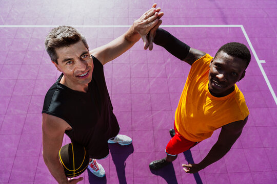 Male athletes give a high five on a purple basketball court
