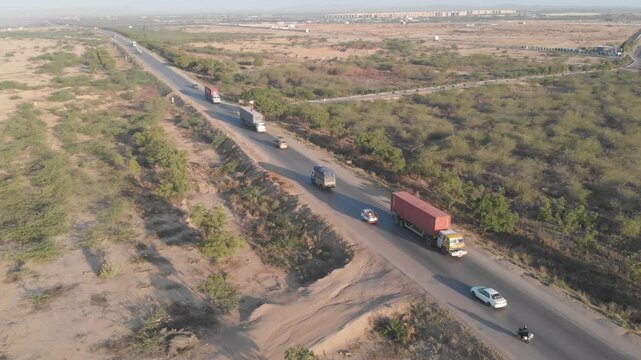 Aerial view of the Makran Coastal Highway winding through the arid desert landscape of the Makran Coastal Range with trucks driving along the road in Pasni, Balochistan, Pakistan.
