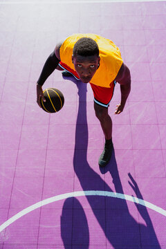 Male basketball player dribbles ball on purple outdoor court