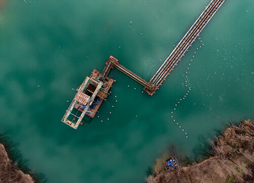 Aerial view of a floating dredger extracting sand and gravel from a flooded quarry, with raw material transported to a processing plant in Milan, Lombardy, Italy.