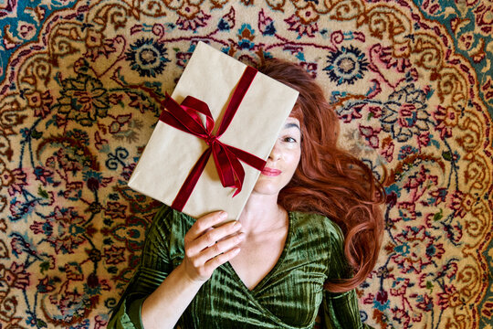 Woman lies on a Persian rug holding a Christmas gift over her face